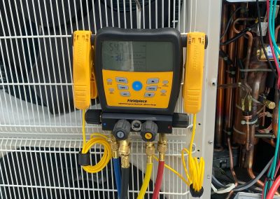 A digital HVAC manifold gauge set is attached to an outdoor air conditioning unit for diagnostics.