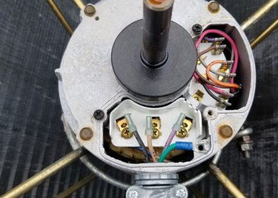 Top view of an exposed electric motor with visible wiring and brass rods in the background.