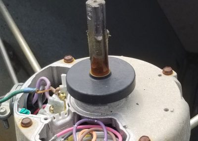 Close-up of an electric motor with exposed wires and a rusted metal shaft.
