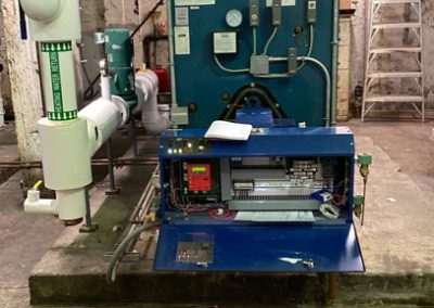 Industrial boiler system in a basement with open control panel and surrounding pipes and gauges.