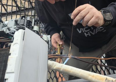 A man uses a torch to solder pipes on an HVAC unit, wearing a black sweatshirt and a smartwatch.