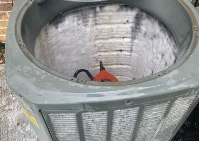 Open air conditioning unit with visible ice buildup inside the coil, next to a brick wall.