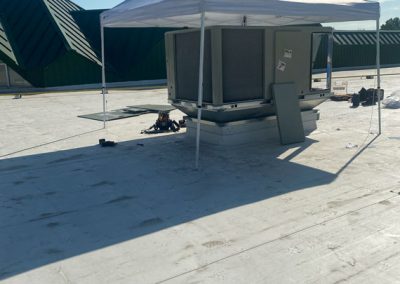 A canopy tent shades rooftop equipment and tools on a flat, sunlit roof with green structures in the background.