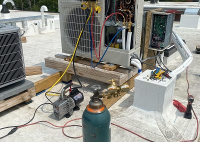 Rooftop HVAC repair setup with tools, gauges, wires, and an oxygen tank on a white roof.
