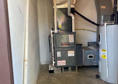 A furnace and water heater are installed in a utility room with exposed pipes and a concrete floor.