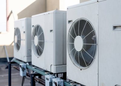 Three white outdoor air conditioning units are mounted in a row on a metal platform.