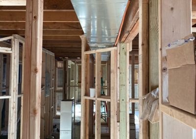 Unfinished house framing with exposed ductwork and wooden studs under construction.