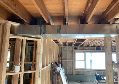 Exposed HVAC ductwork in a house under construction with unfinished wooden framing and ceiling beams.
