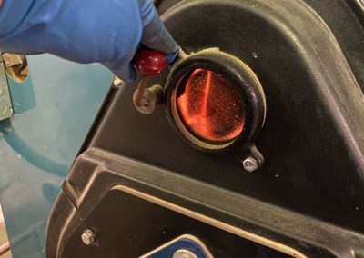 A gloved hand opens a small hatch to reveal a glowing red interior of industrial equipment.