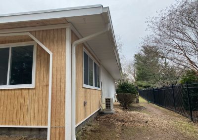 Side view of a single-story house with wood panel siding, white trim, and a fenced yard on a cloudy day.