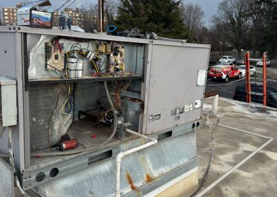 An HVAC unit on a rooftop with its panel open, exposing internal wiring and components, under a cloudy sky.
