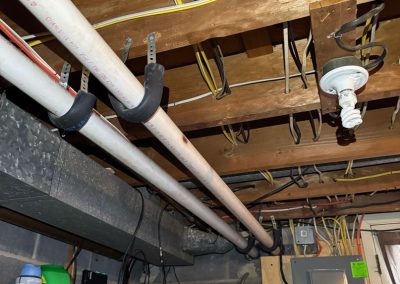 Basement ceiling with exposed pipes, electrical wires, a light fixture, meter, and breaker panel.