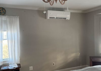 A bedroom with gray walls, a chandelier, a bed, a nightstand, and a wall-mounted air conditioner.