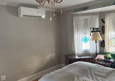 Bright bedroom with gray walls, chandelier, bed, air conditioner, and light coming through windows with sheer curtains.
