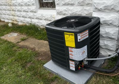 Outdoor air conditioning unit installed next to a house with siding and brick exterior.
