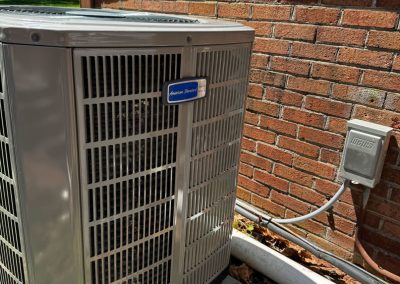 Outdoor air conditioning unit next to a brick wall with electrical wiring and vent pipe nearby.