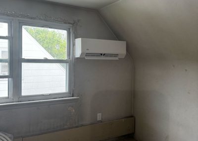 Small room with a slanted ceiling, window, wall-mounted AC, stained carpet, and peeling paint on the window frame.