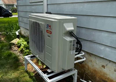 A heat pump unit mounted on a metal stand outside a house, with cables and pipes connected.