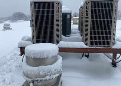 Snow-covered air conditioning units on a rooftop during winter, surrounded by a thick layer of snow.