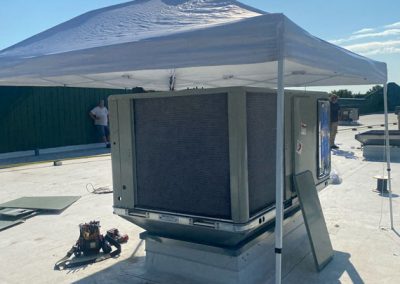 Large HVAC unit under a canopy on a rooftop, with tools and a person nearby on a sunny day.