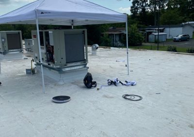 A rooftop HVAC unit under a canopy, with tools and equipment scattered on the white roof surface.
