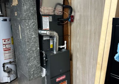 A Goodman furnace and ductwork installed in a basement utility area near a water heater.