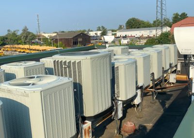Row of large air conditioning units on a rooftop under a clear blue sky, with buildings in the background.