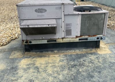 Large rooftop HVAC unit on a flat, gravel-lined roof with green metal buildings in the background.