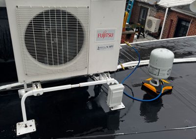 An outdoor Fujitsu AC unit and refrigerant tank are set up on a wet rooftop in a city.