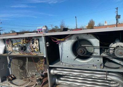 Open HVAC unit with exposed wiring, circuit boards, and blower fan components under a clear sky.