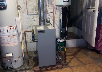 A furnace and water heater in a basement with exposed pipes and tiled floor.