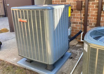 Gray outdoor air conditioning unit next to a brick wall and another AC unit on a concrete pad.