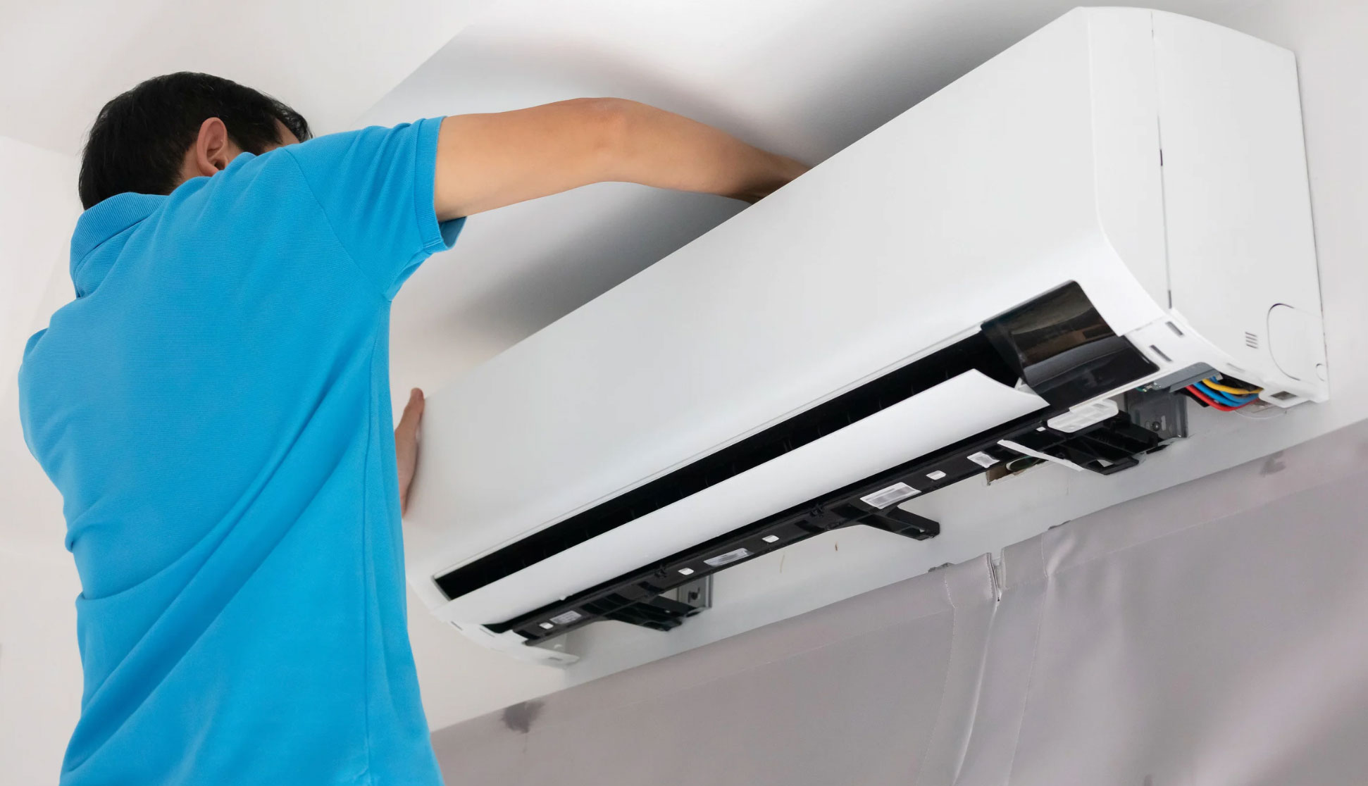 Person in blue shirt installing or repairing a wall-mounted air conditioner indoors.