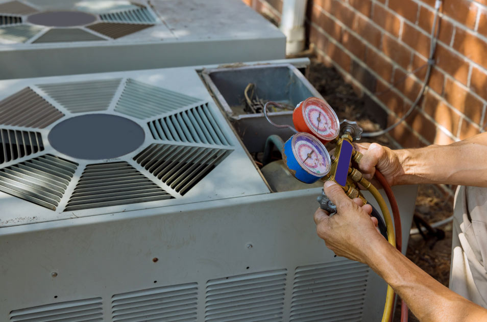 Technician using gauges to check an outdoor air conditioning unit next to a brick wall.