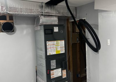A large HVAC unit with exposed ducts and wires is installed in a partially finished room with gray walls.
