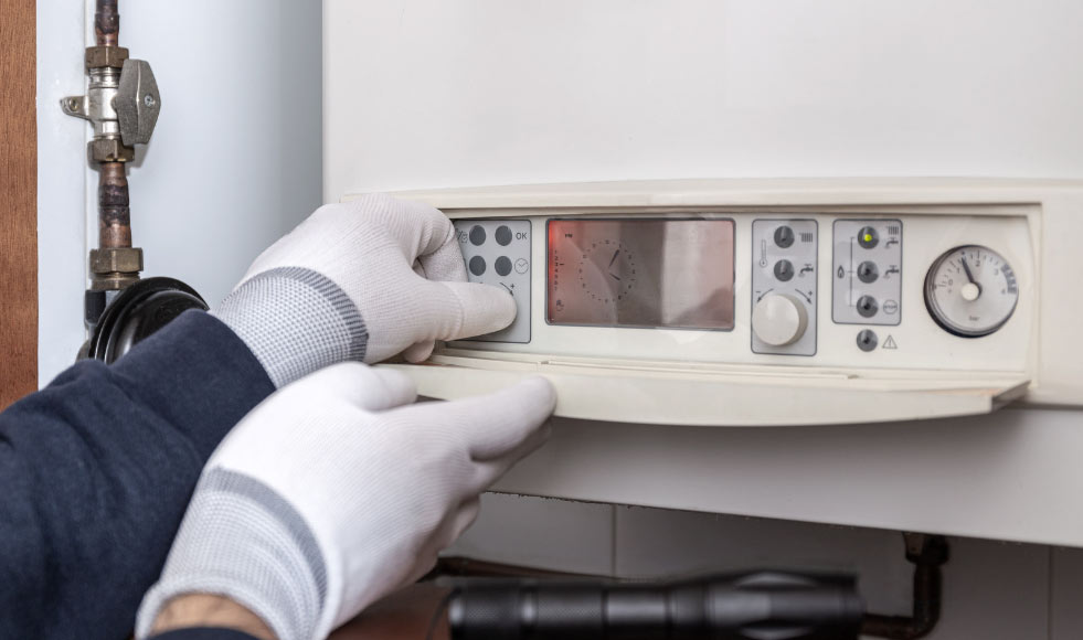 Gloved hands adjusting controls on a white boiler or heating system panel.