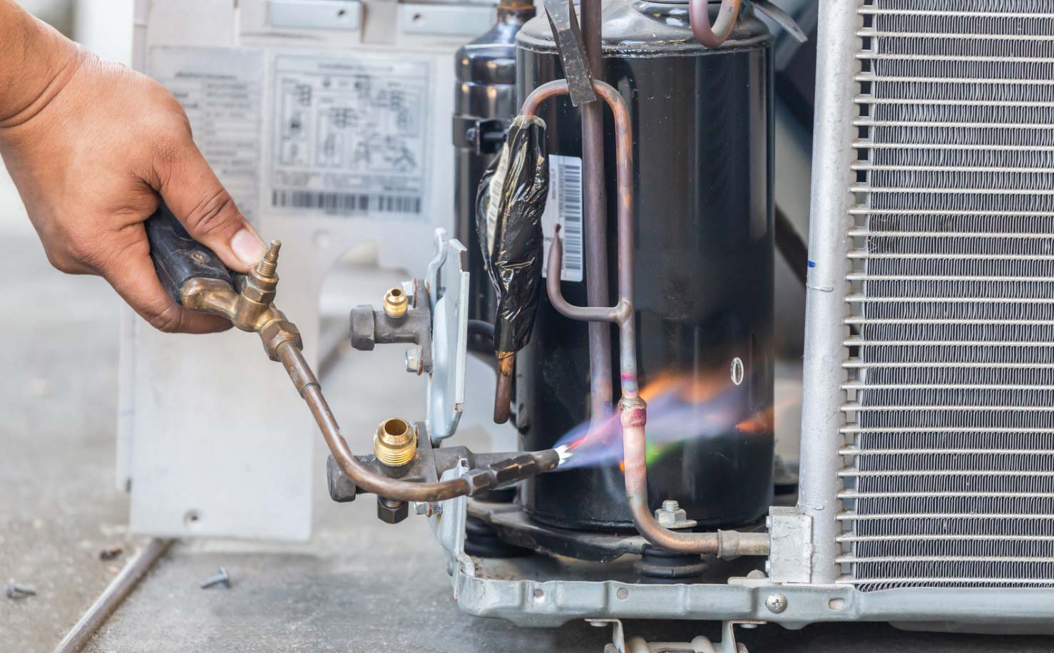 A person uses a blowtorch to repair or weld pipes in an air conditioning unit.