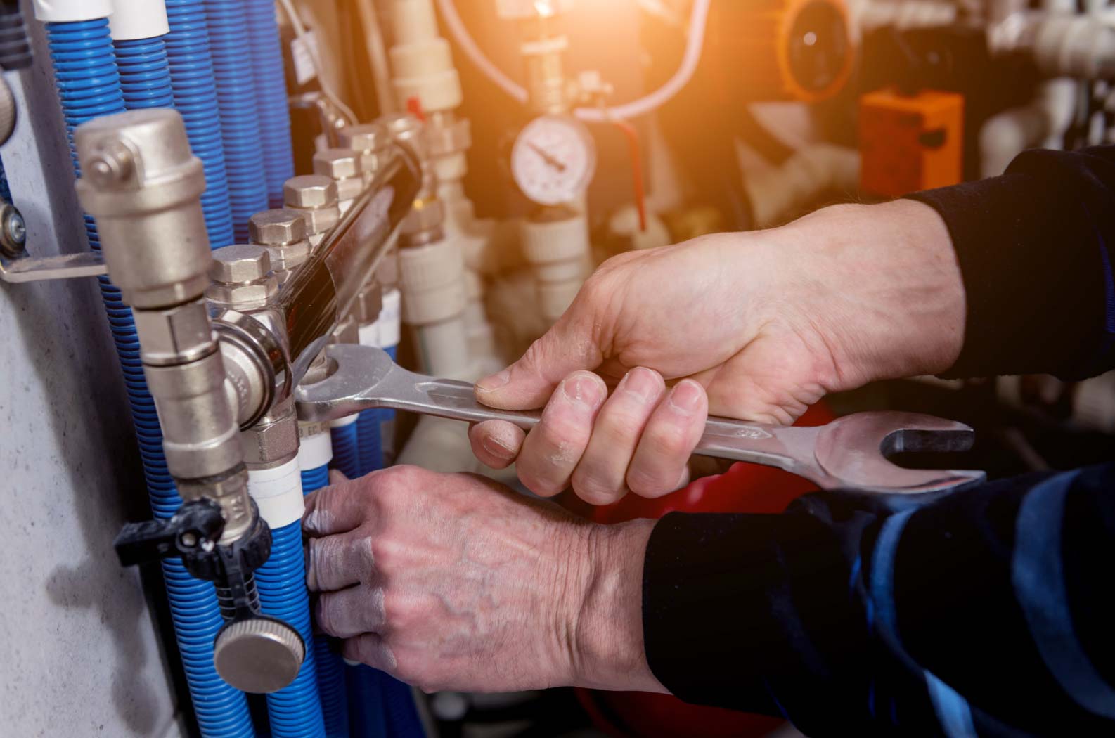 Person using a wrench to adjust pipes and valves in a plumbing or heating system, with blue tubing visible.