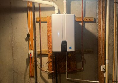 Tankless water heater mounted on a basement wall with connected pipes and visible wiring.